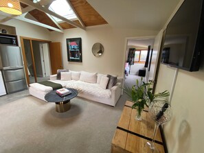 A living room with a white sofa, a coffee table, and a wooden side table with a vase and glass. - Resort Arrowtown (Speargrass Flat)