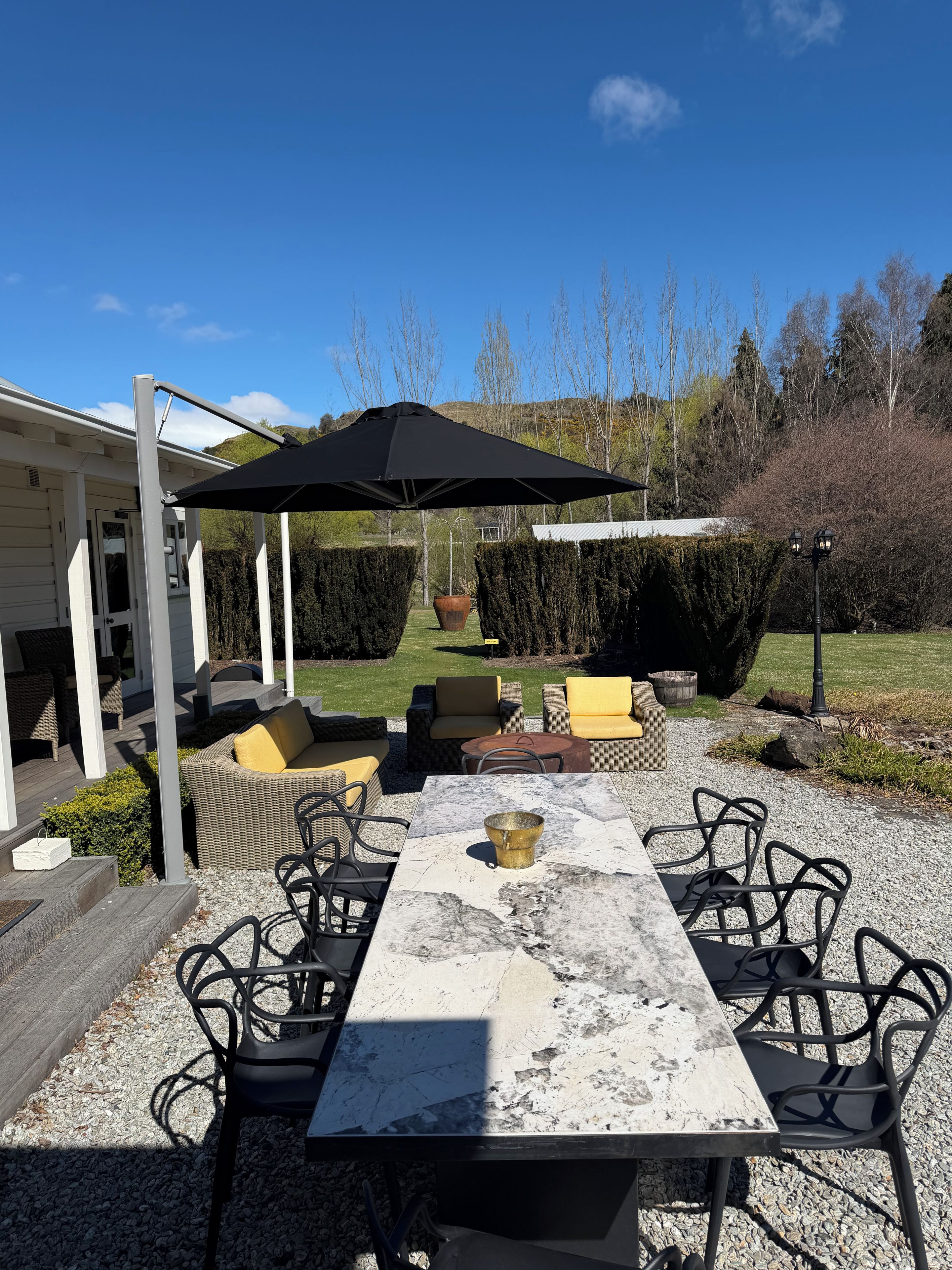 An outdoor patio with a table, chairs, and a pergola with a black umbrella.