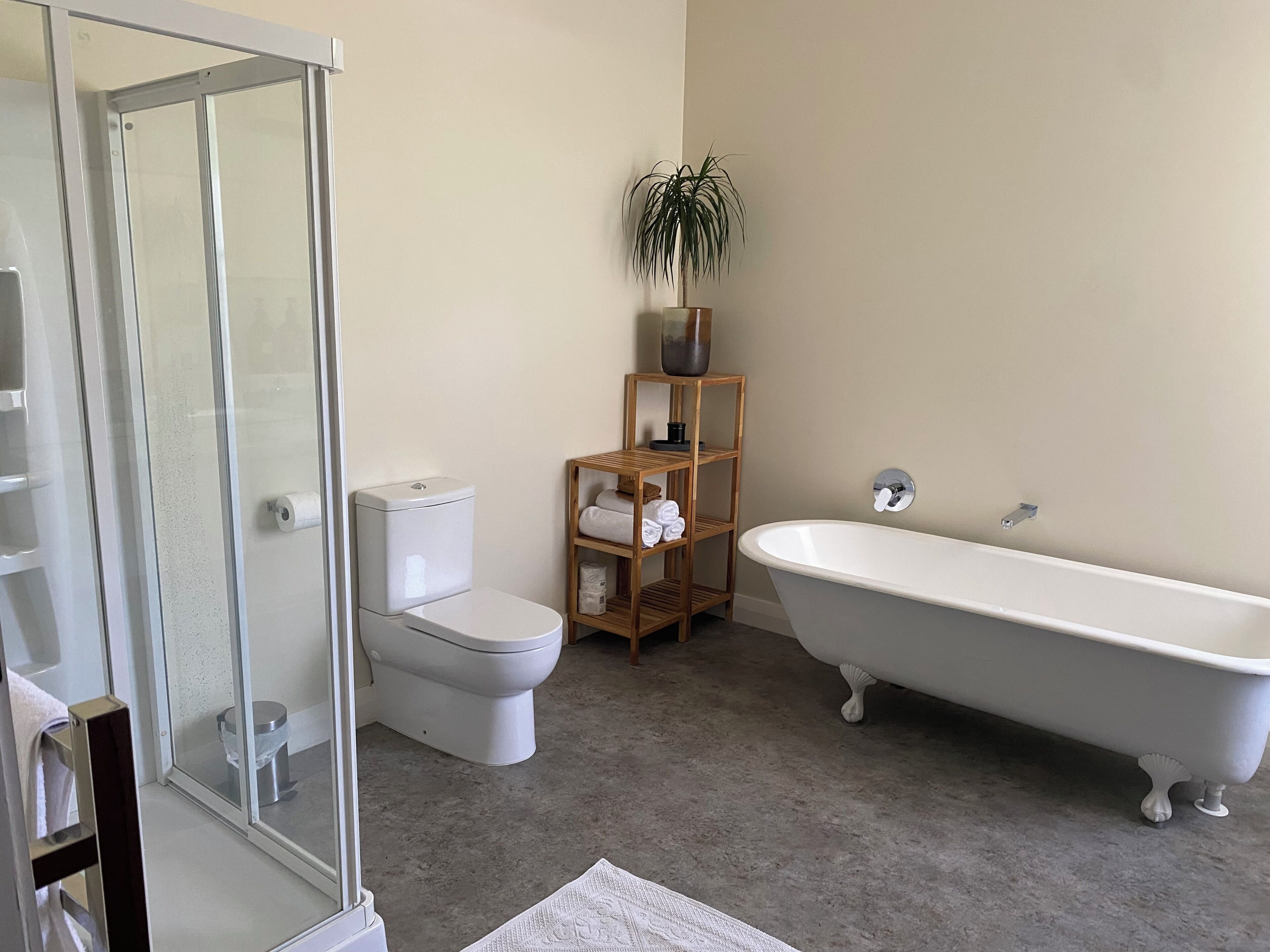 A bathroom with a glass shower enclosure, a toilet, a freestanding bathtub, and a wooden shelf with towels.