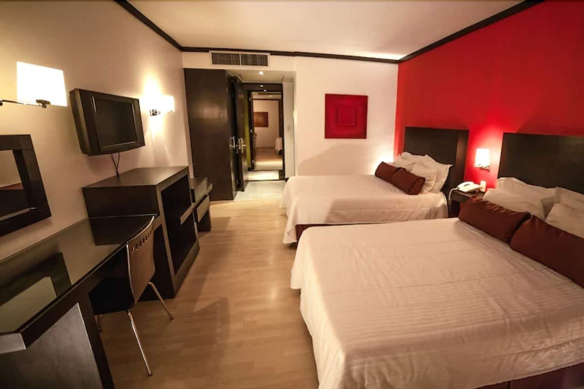 Habitación de hotel con dos camas, un escritorio, un televisor y una pared de acento roja.
