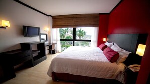 A modern hotel room with a large bed, a desk with a chair, a television, and a window with a view of palm trees. - Hotel Inglaterra (Tampico)