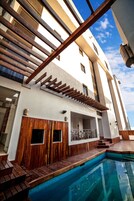 Un edificio moderno con piscina, terraza de madera y una escalera que lleva a un balcón.