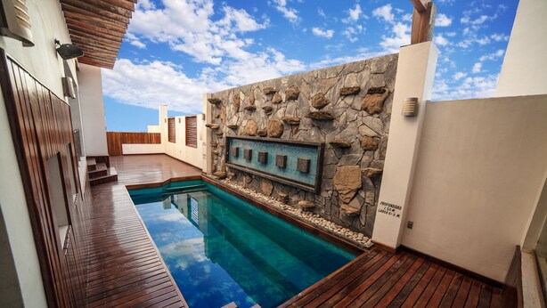 A swimming pool with a wooden deck, a stone wall with a mosaic, and a clear blue sky. - Hotel Inglaterra (Tampico)