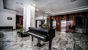 A grand piano in a spacious lobby with marble flooring, a reception desk, and a modern elevator. - Hotel Inglaterra (Tampico)