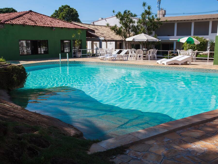 Una piscina amb gandules i ombrel·les, envoltada d'un edifici amb teulada ceràmica i una paret verda.