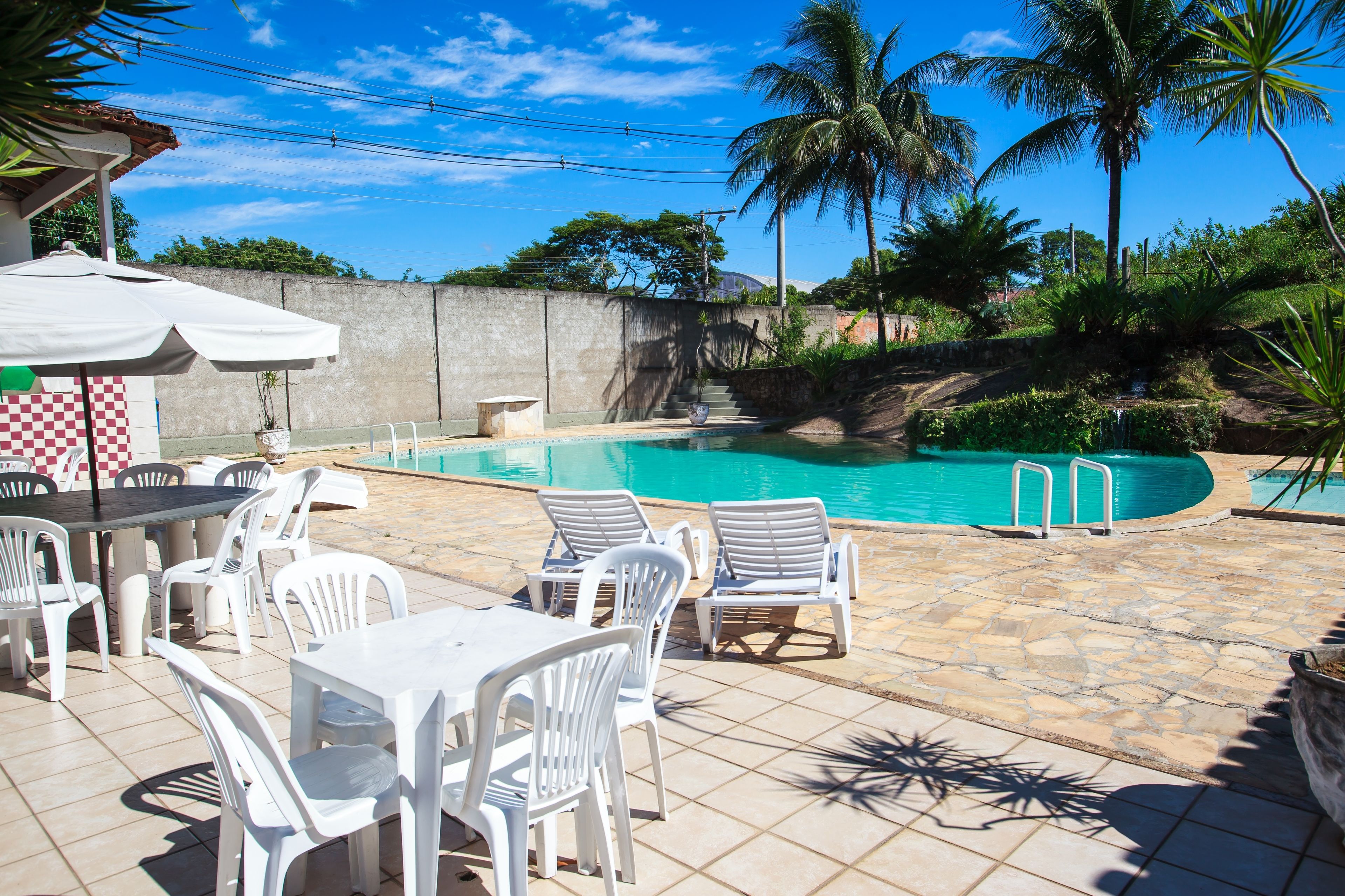 A swimming pool area with lounge chairs and a table, surrounded by palm trees and a stone wall.