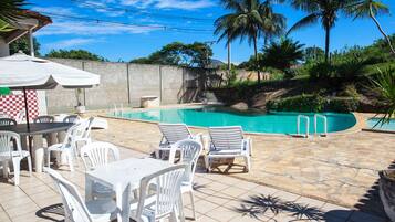 Un espace piscine aménagé avec des chaises longues et une table, entouré de palmiers et d’un mur de pierre.