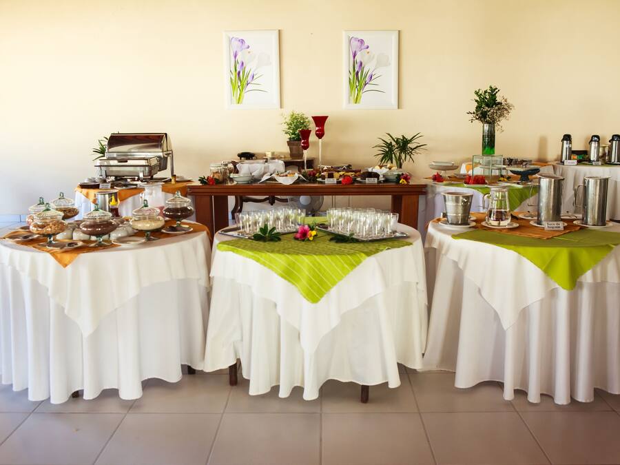 A buffet setup with multiple tables covered in white tablecloths, featuring food containers, glassware, and a coffee station.