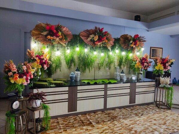 Zona de recepción con mostrador, plantas decorativas y alfombra estampada.