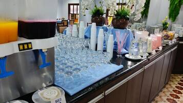 Disposição de buffet com dispensador de bebidas, pratos empilhados e diversos tipos de copos.