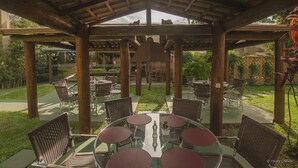 An outdoor patio with round tables and wicker chairs, surrounded by a wooden pergola structure. - SJ Jaguariaíva - San Juan Jaguariaíva (Jaguariaíva)