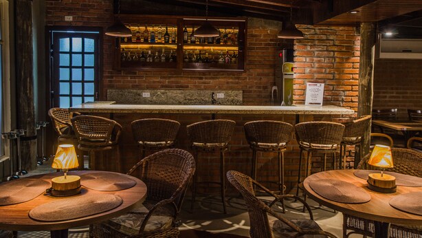 A bar area with wicker chairs and tables, a brick wall, and a bar counter with bottles. - SJ Jaguariaíva - San Juan Jaguariaíva (Jaguariaíva)