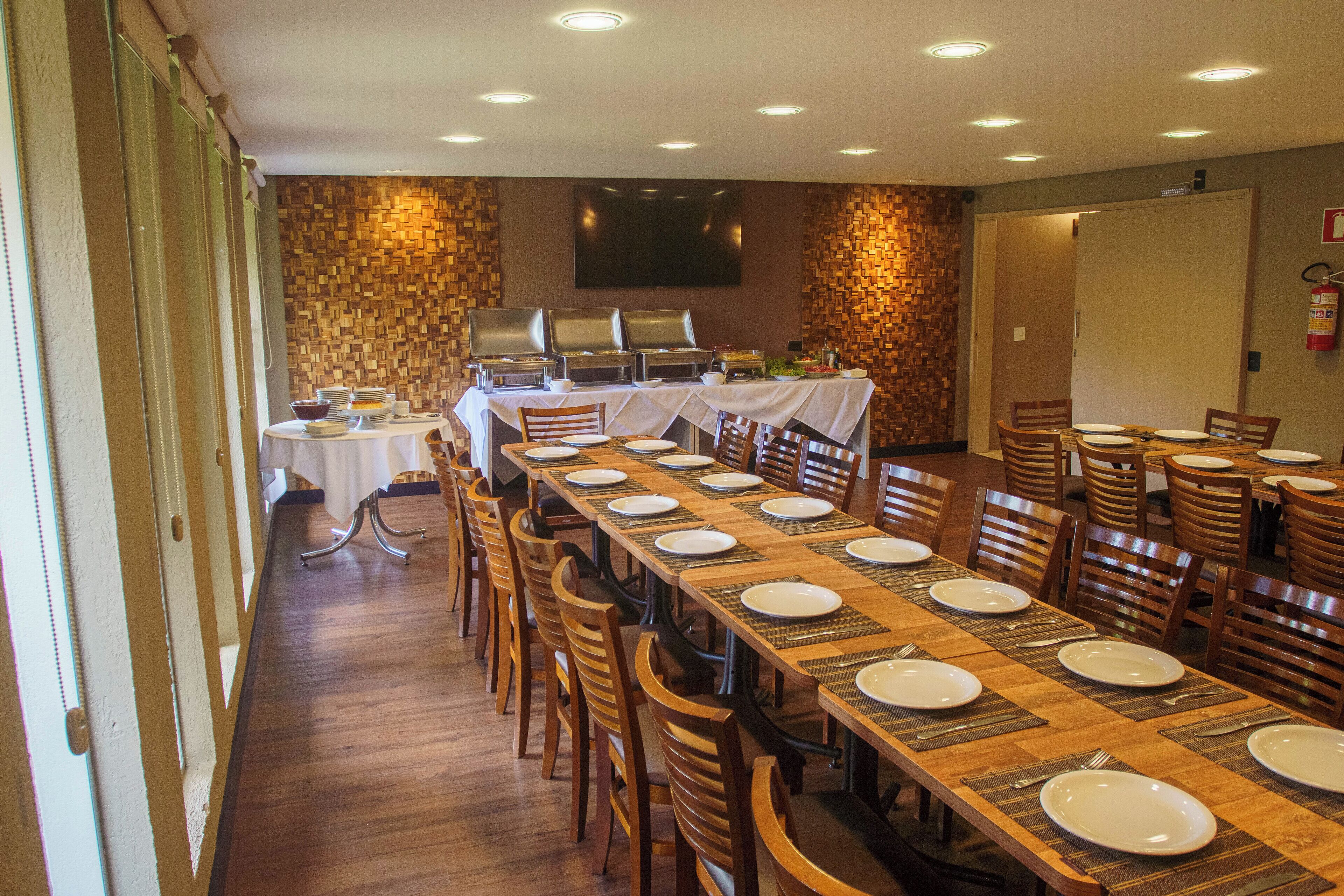 Un comedor con una mesa larga dispuesta para varias personas, sillas, una estación de buffet y un extintor en la pared.