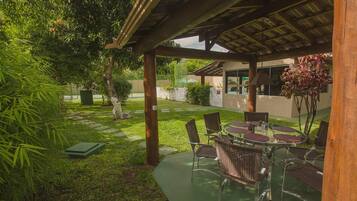 Un patio exterior con zona de estar cubierta, rodeado de abundante follaje y un sendero.