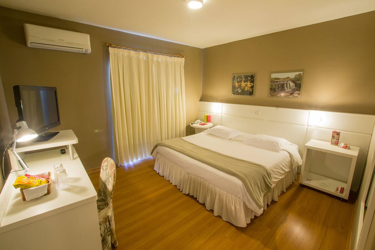 Une chambre d’hôtel équipée d’un lit, d’une table de chevet, d’une télévision et d’un bureau avec une lampe et un panier de collations.