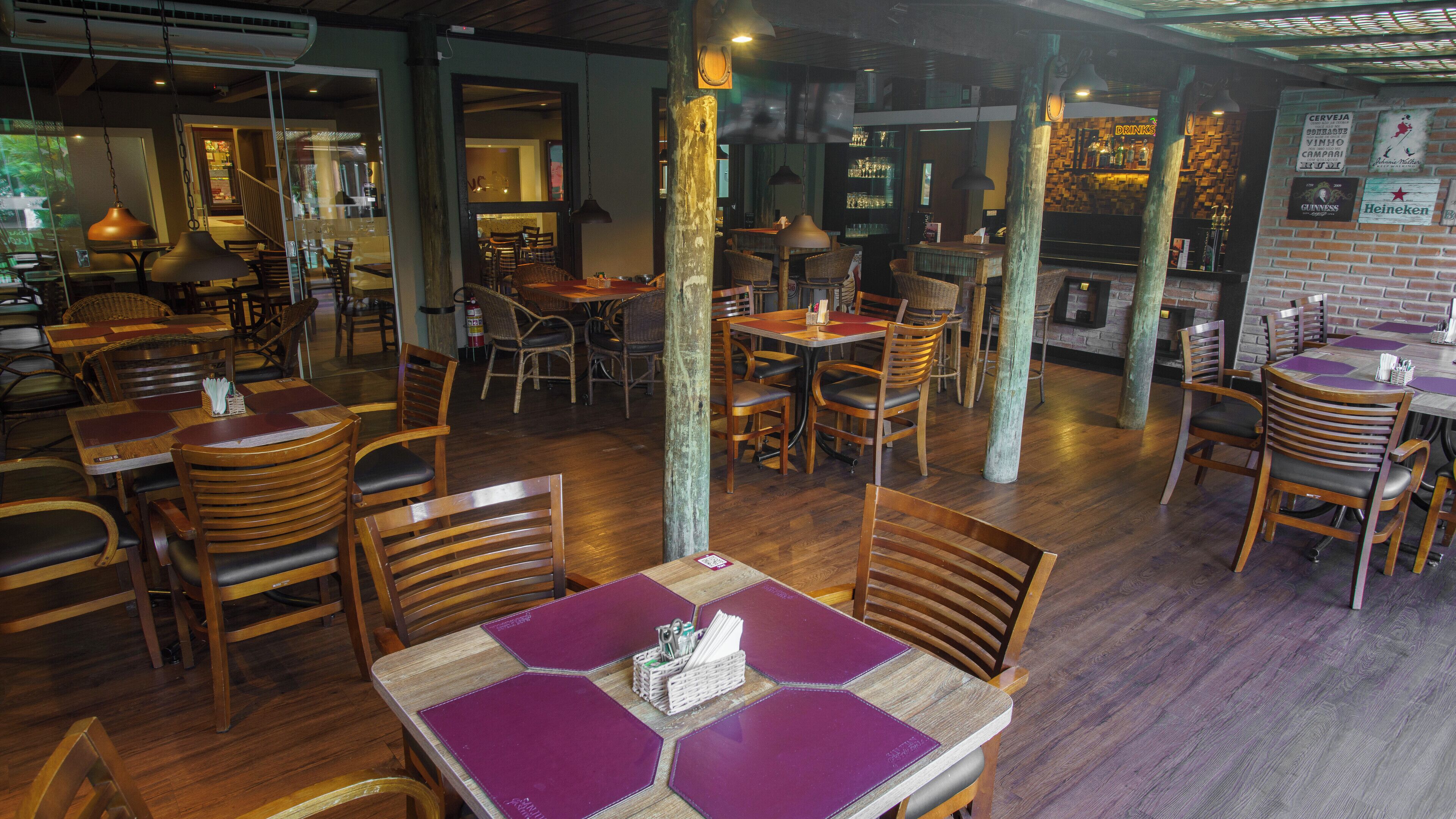 A restaurant with wooden tables and chairs, a bar area, and a brick wall with drink labels.