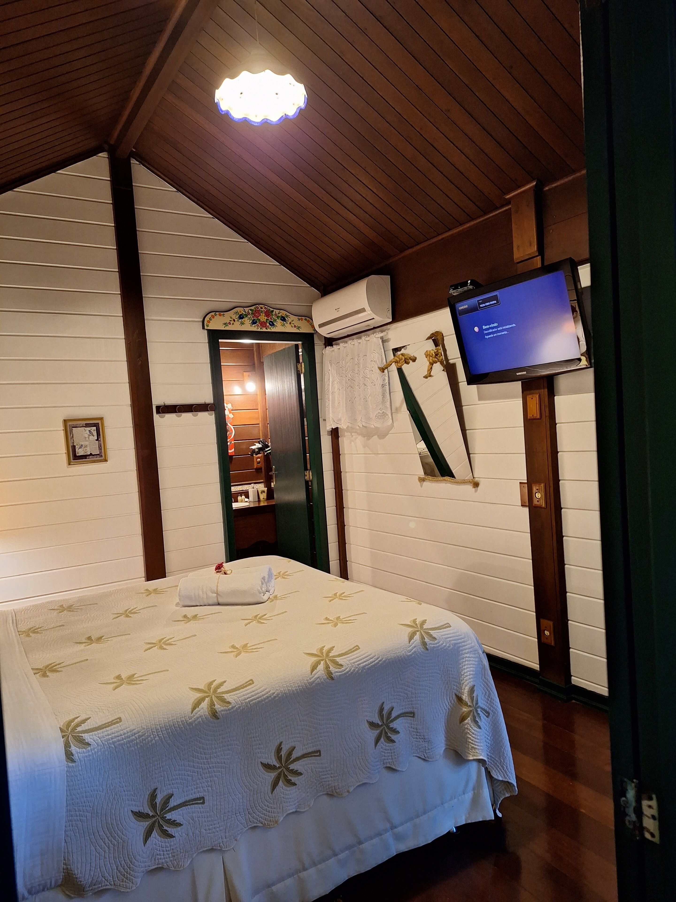 Habitación de hotel con cama, televisor, aire acondicionado y techo de madera.