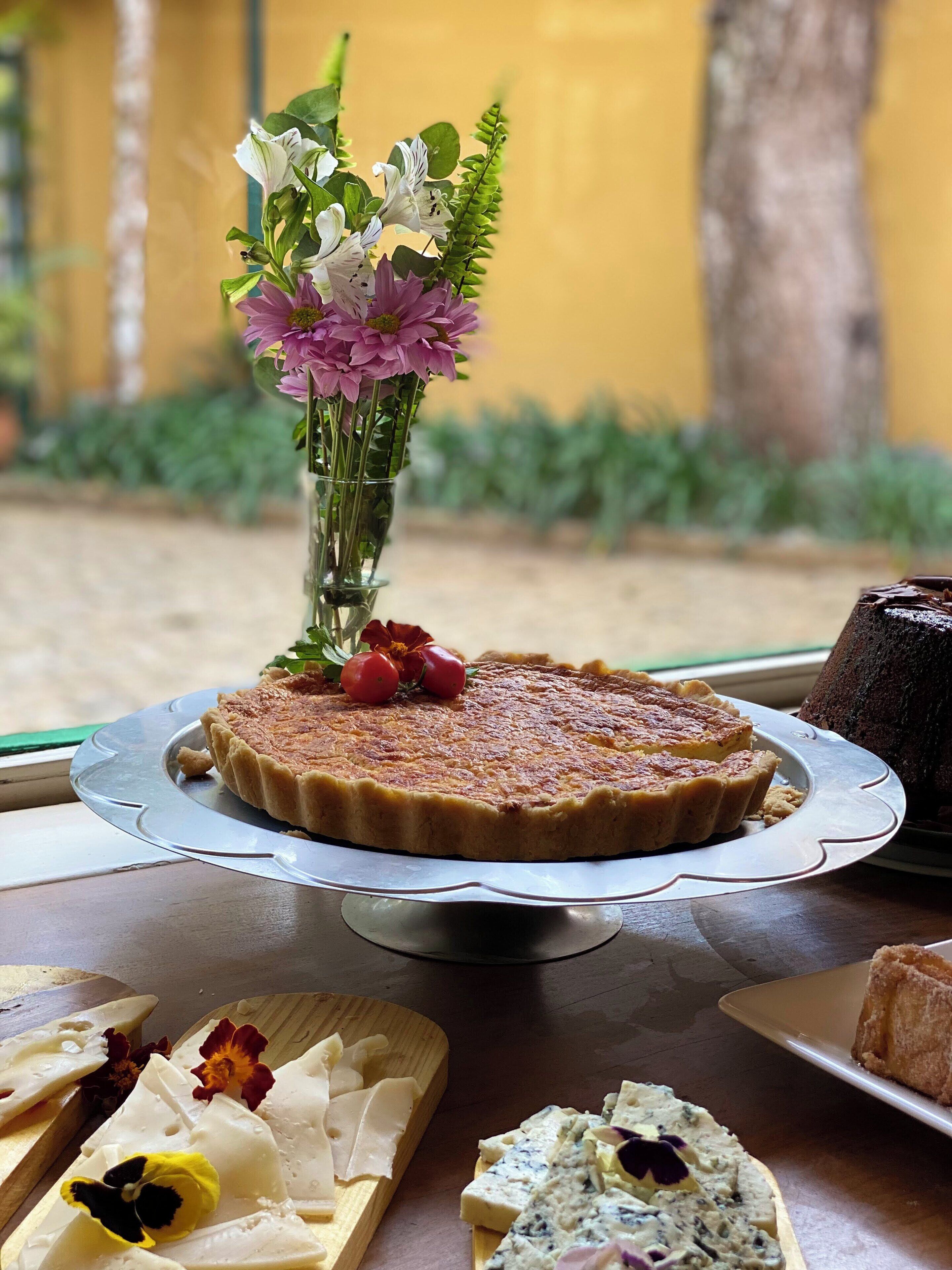 A dessert table with a quiche, a cake, and various cheeses, accompanied by a floral arrangement.