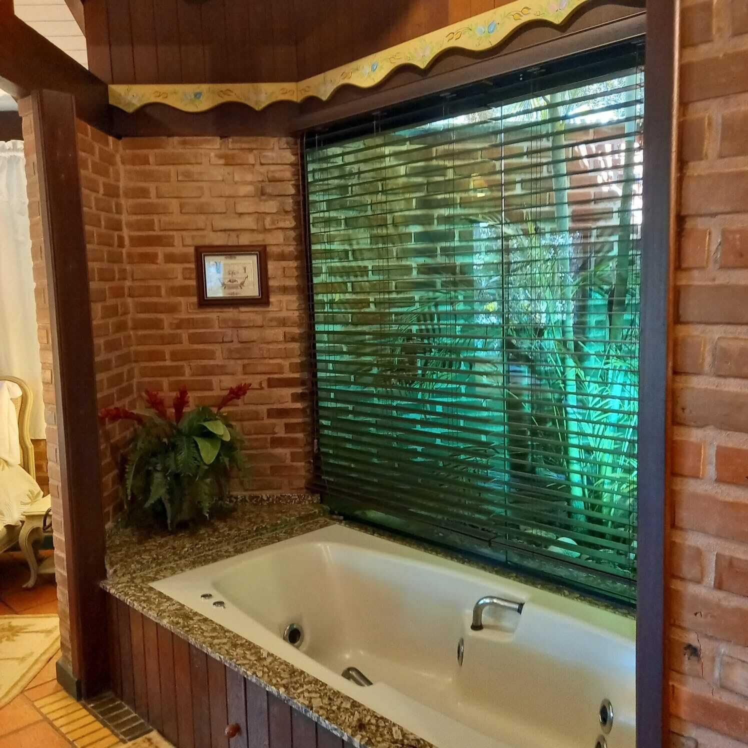 Un baño con un ventanal grande cubierto por persianas, un lavamanos y un cuadro en la pared.