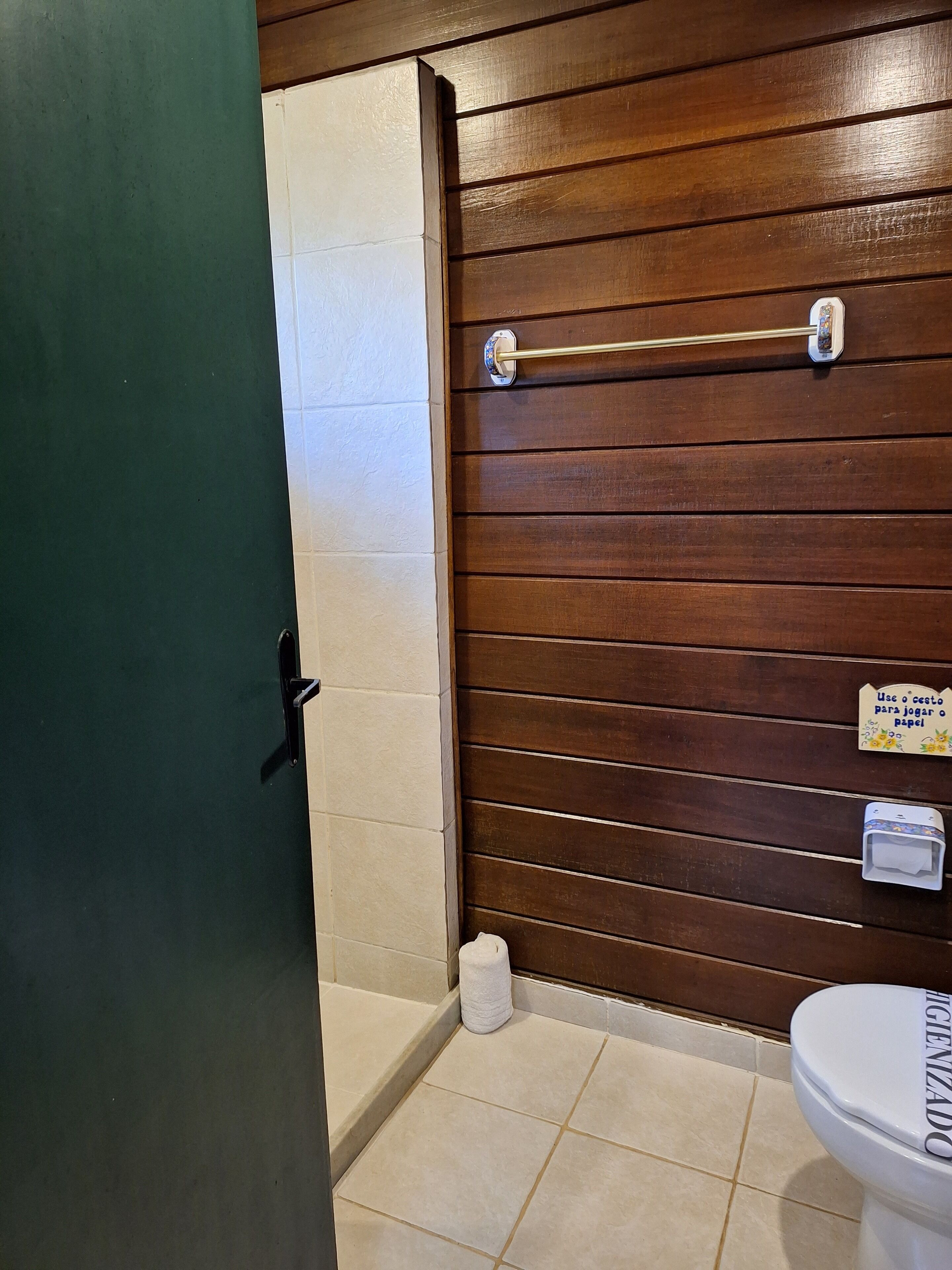 A bathroom with a wooden wall, a toilet, a towel dispenser, and a toilet paper holder.