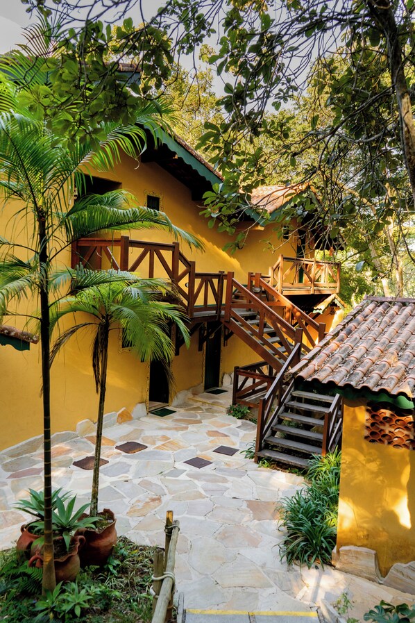 Un patio con un edificio amarillo, una escalera de madera y plantas en macetas.