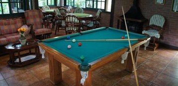 Una mesa de billar en una habitación con chimenea, un sofá y varias sillas.