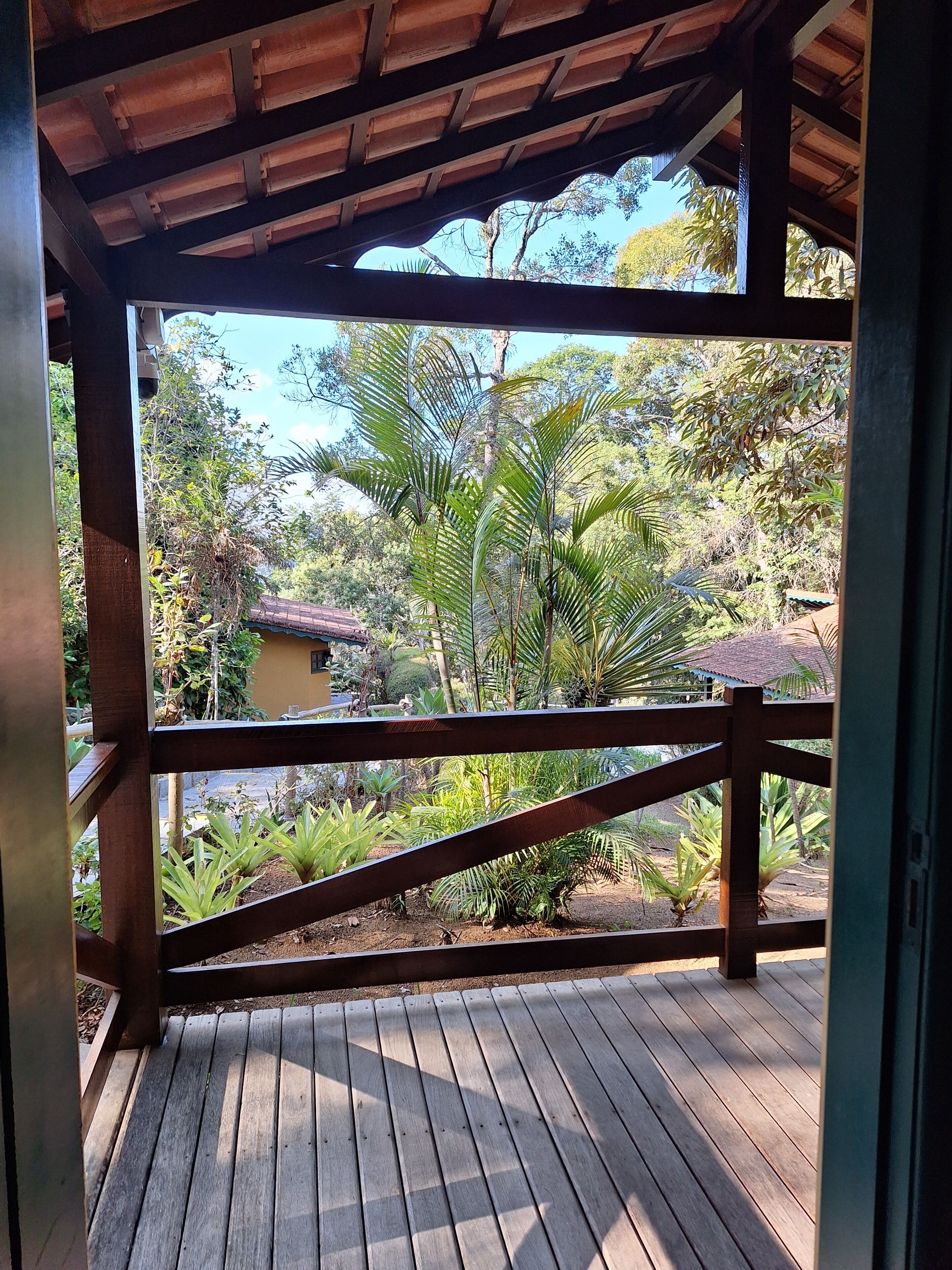 A wooden deck with a view of a lush garden and a building in the background.