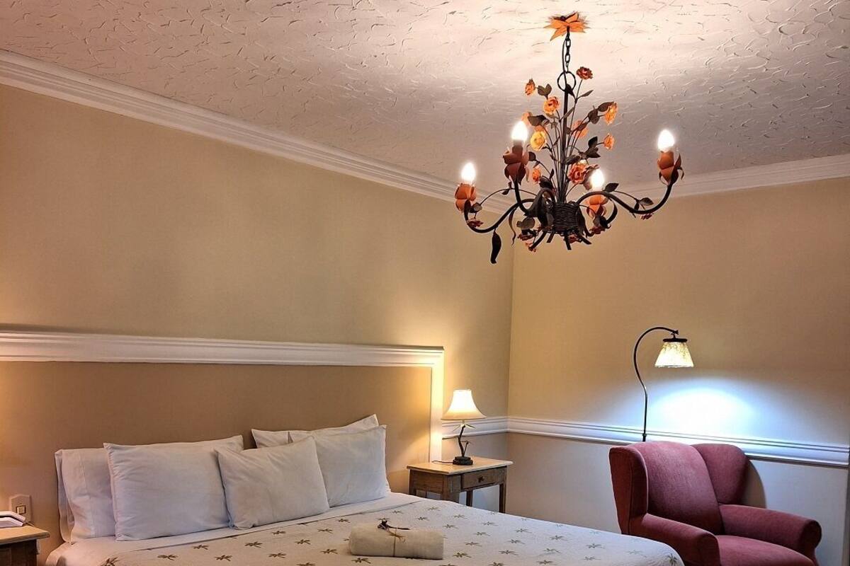Een slaapkamer met een bed, nachtkastje, stoel, lamp en een kroonluchter.