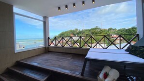 A balcony with a view of the sea and a cityscape, featuring a wooden bench and a small table with a basket. - Charme Pousada Boutique & Spa (Cairu)
