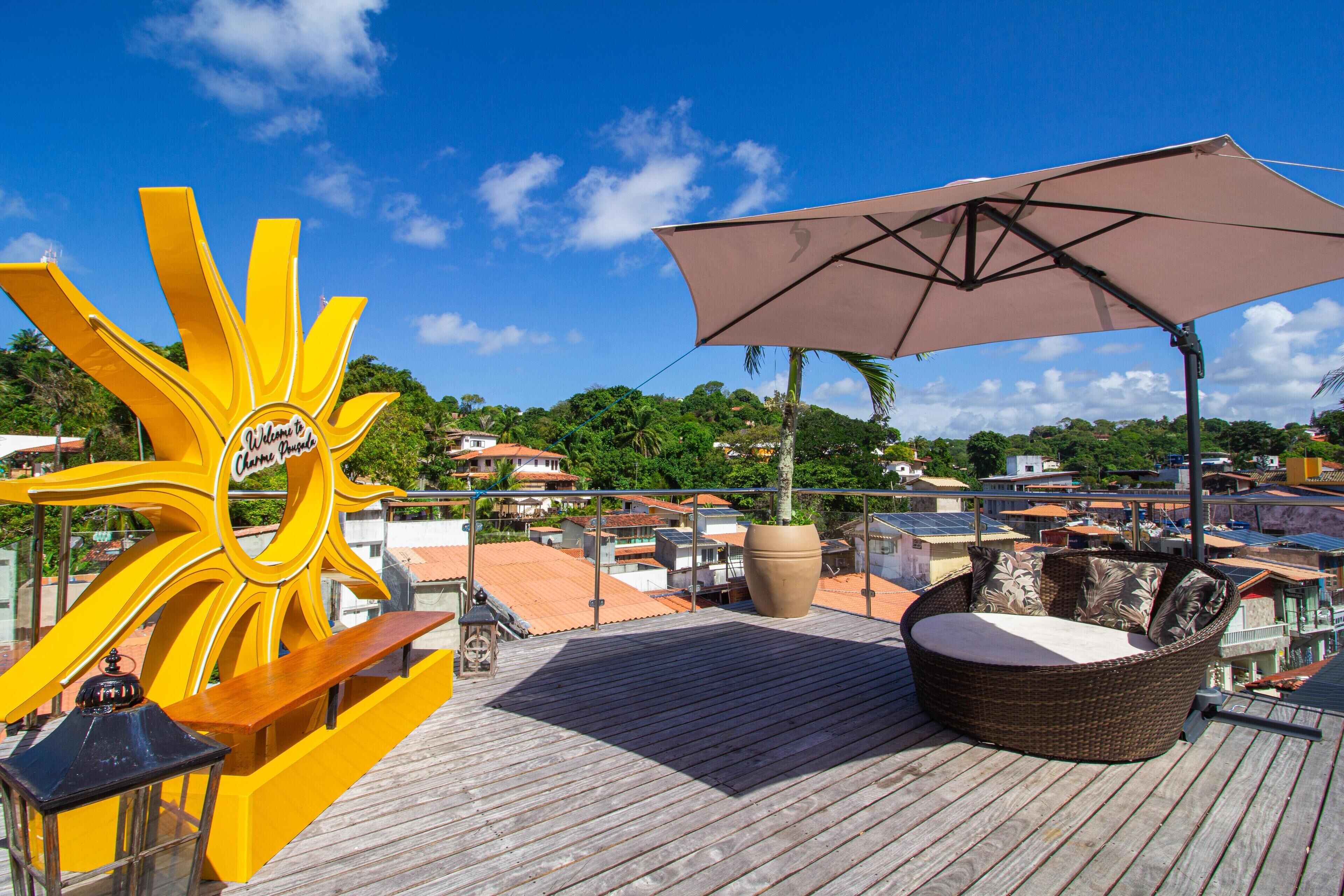 A rooftop deck with a sun-shaped sign, a large umbrella, and a wicker sofa.
