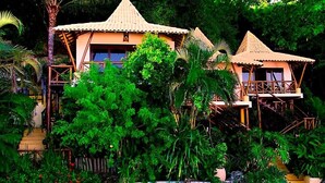 A resort with multiple bungalow-style buildings, each with a thatched roof and surrounded by lush greenery. - Charme Pousada Boutique & Spa (Cairu)