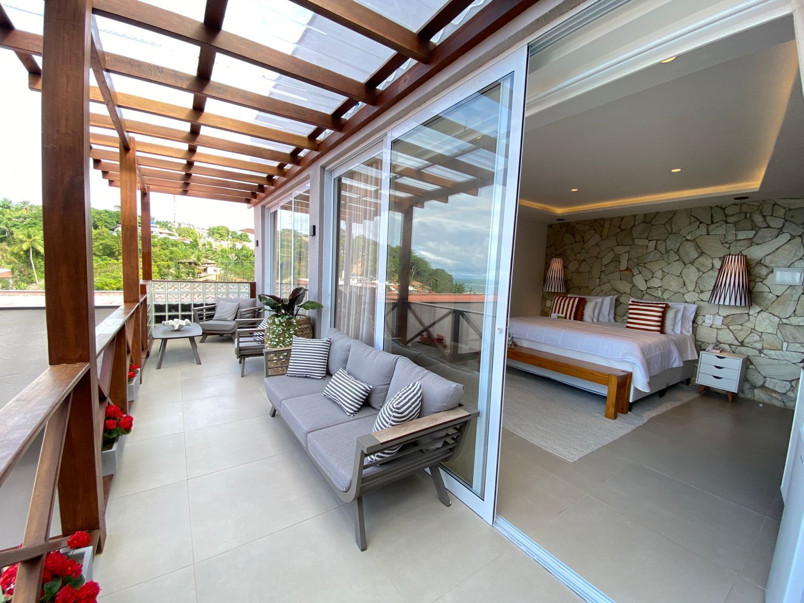 Quarto de hotel moderno com parede de pedra, varanda com pérgola de madeira, sofá e cama.