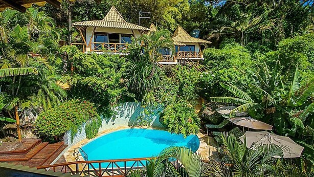 A pool surrounded by lush greenery, wooden deck, and thatched-roof structures. - Charme Pousada Boutique & Spa (Cairu)