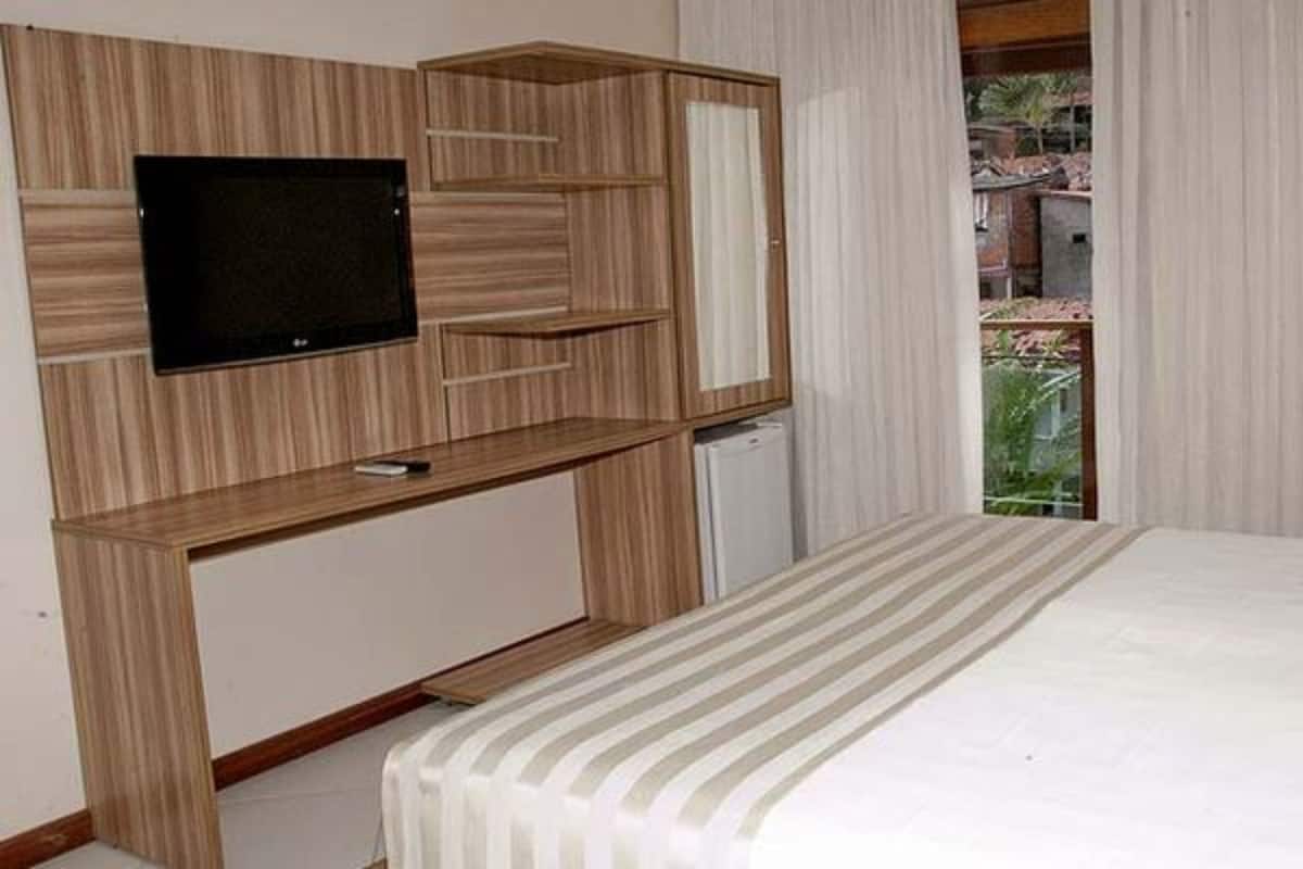 Un dormitorio con una cama, un televisor montado en un mueble de madera y una ventana con cortinas.