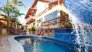 Una piscina con una cascada, rodeada por una terraza de madera y palmeras.
