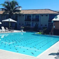 Una piscina con carril delineado, sillas de descanso, sombrillas y una palmera.