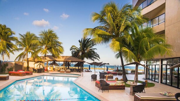 Un espace aménagé au bord de la piscine, avec des chaises longues, des parasols et des palmiers.