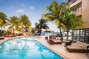 Ein Poolbereich mit Liegestühlen, Sonnenschirmen und Palmen.