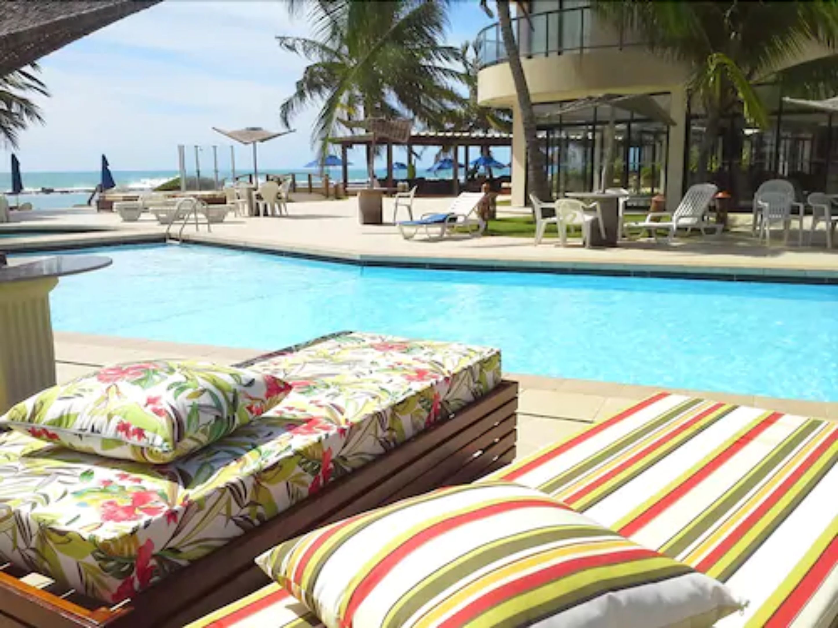 Área de piscina com cadeiras de descanso e vista para o oceano.