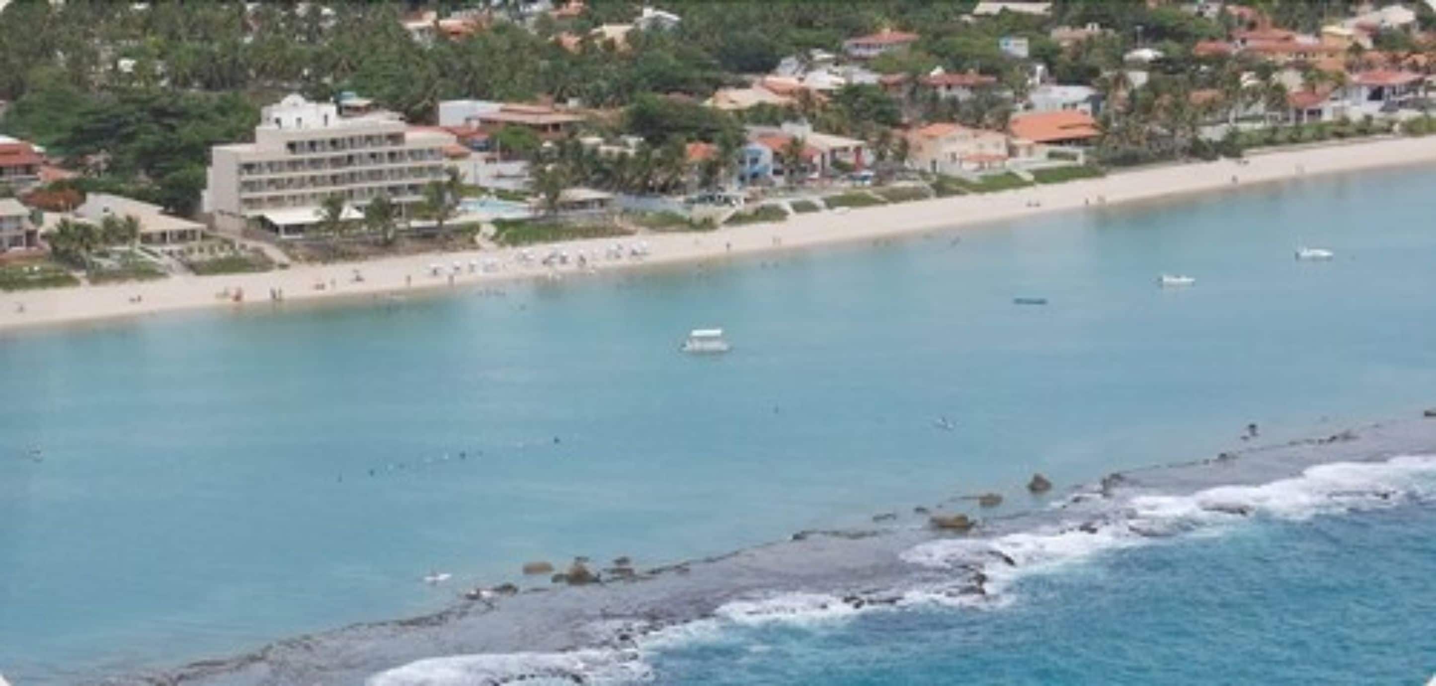 A coastal area with a beach, a hotel with multiple floors, and a clear view of the sea.