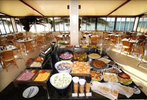 Ein reichhaltiges Buffet in einem geräumigen Raum mit Tischen und Stühlen, großen Fenstern und Blick auf den Ozean.