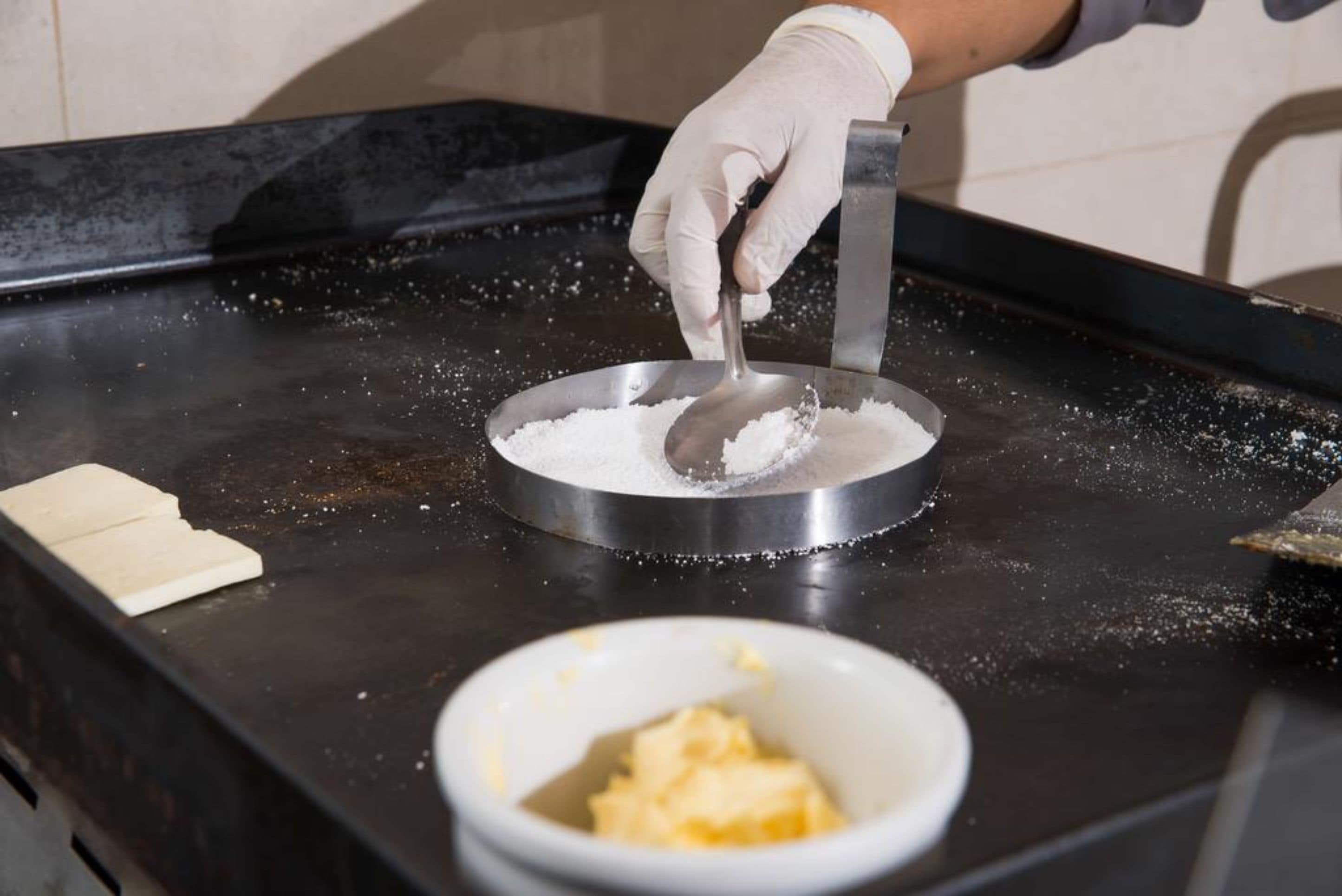 A person scooping white powder from a metal container onto a black surface.