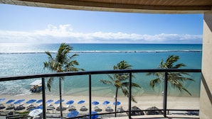Un balcon avec vue sur une plage, des palmiers et une eau d’un bleu cristallin.