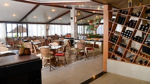 Un restaurant avec des chaises et des tables en osier, un présentoir à bouteilles de vin et une vue sur la mer.