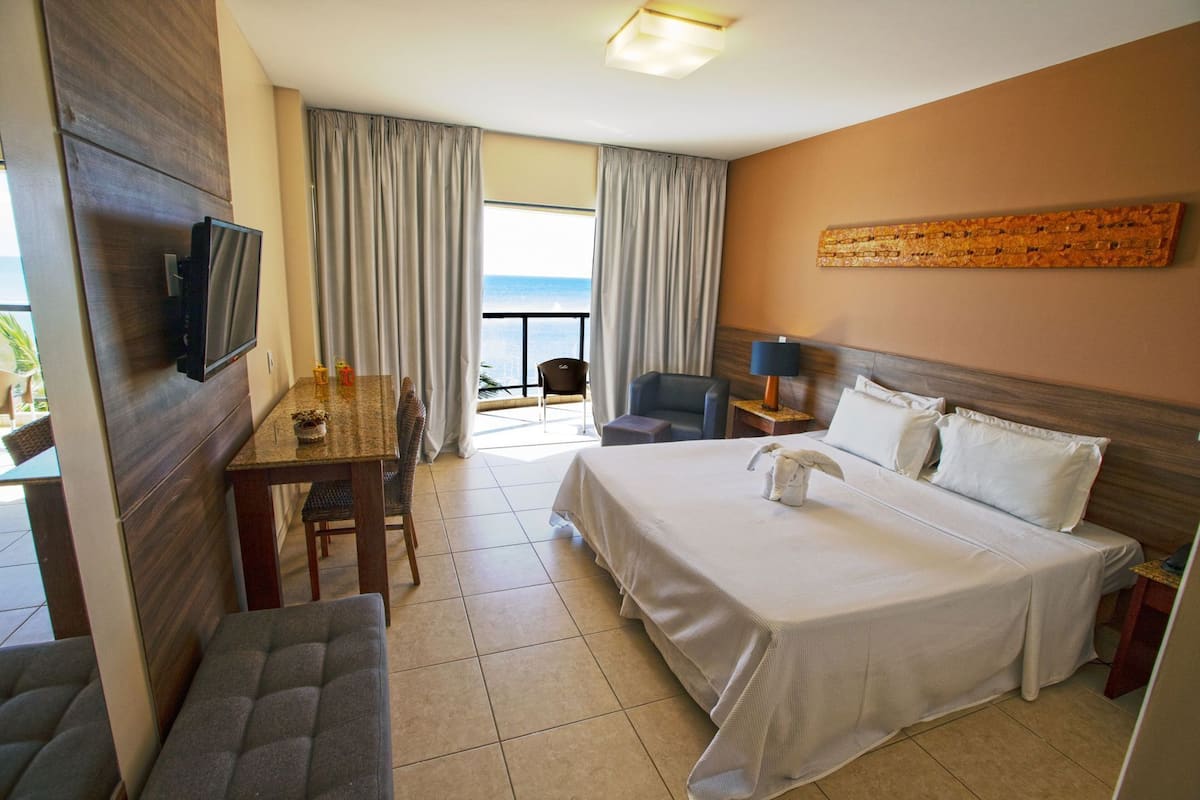 Habitación de hotel con cama, escritorio, silla, televisión y vista al océano.
