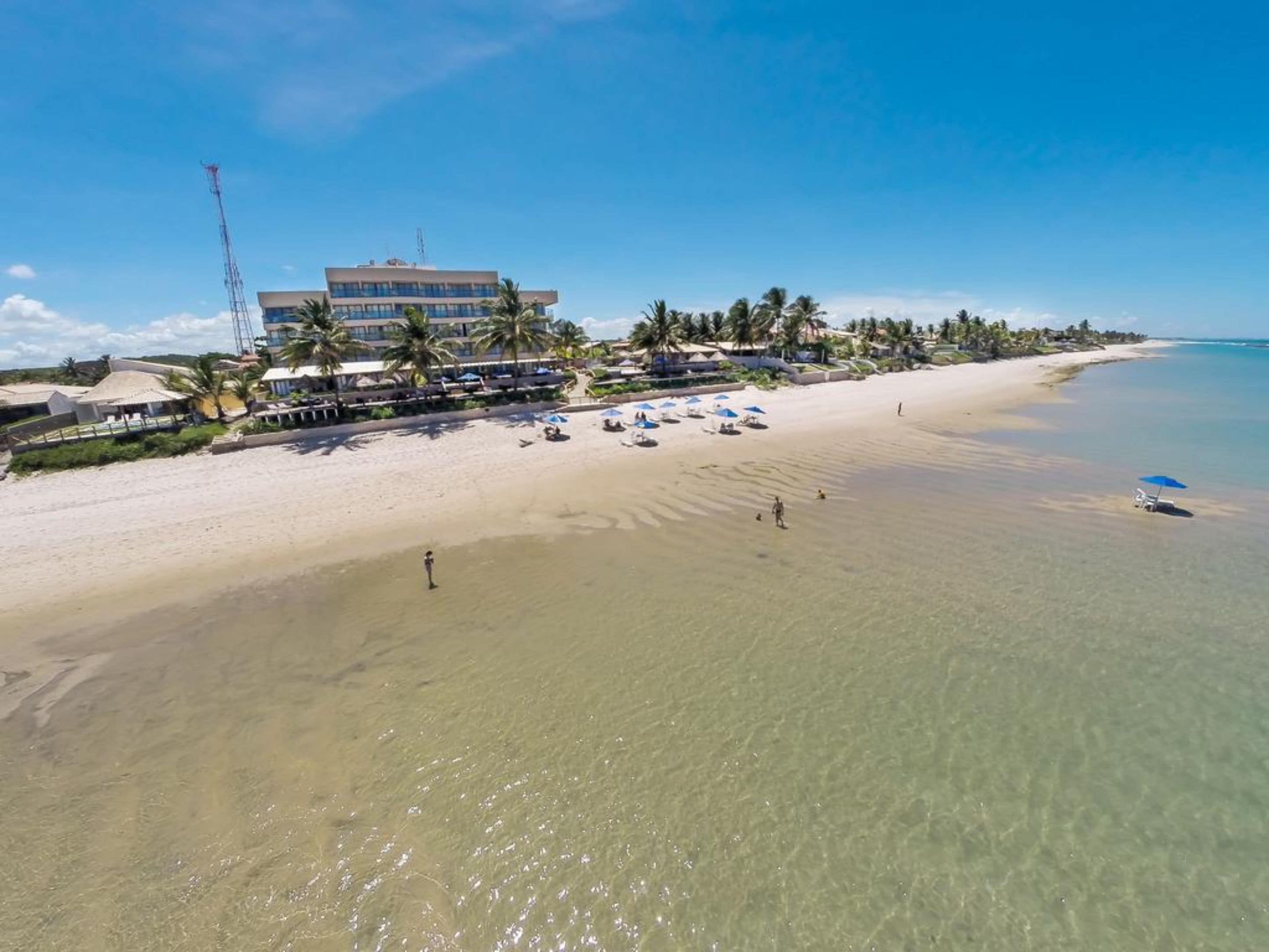 A beach resort with a large building, palm trees, and clear blue water.