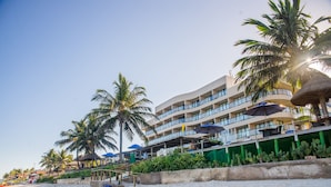 Un hôtel en bord de mer doté de nombreux balcons, de palmiers et de parasols.