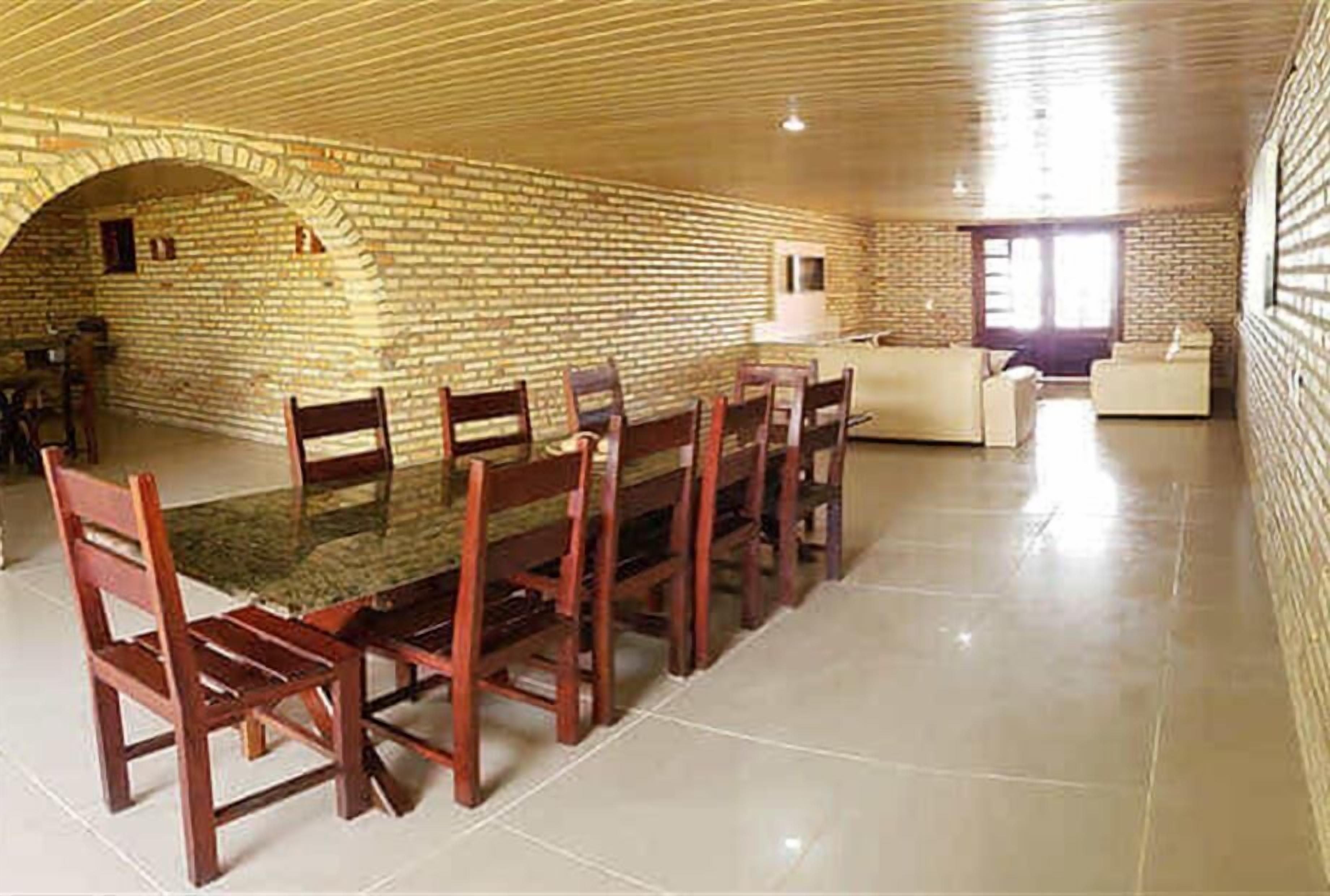 A dining area with a brick wall, a long table with chairs, and a sofa in the background.