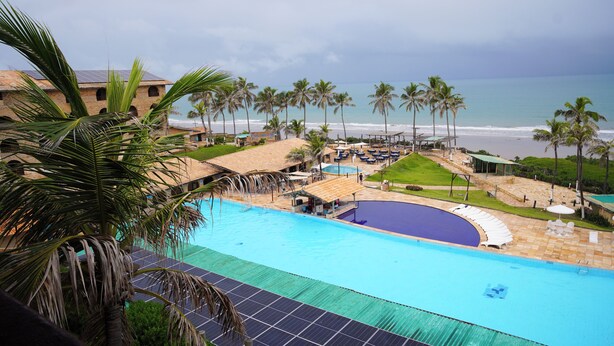 Un resort con piscina, vista a la playa, palmeras y un edificio con el letrero 'Cousin's'.