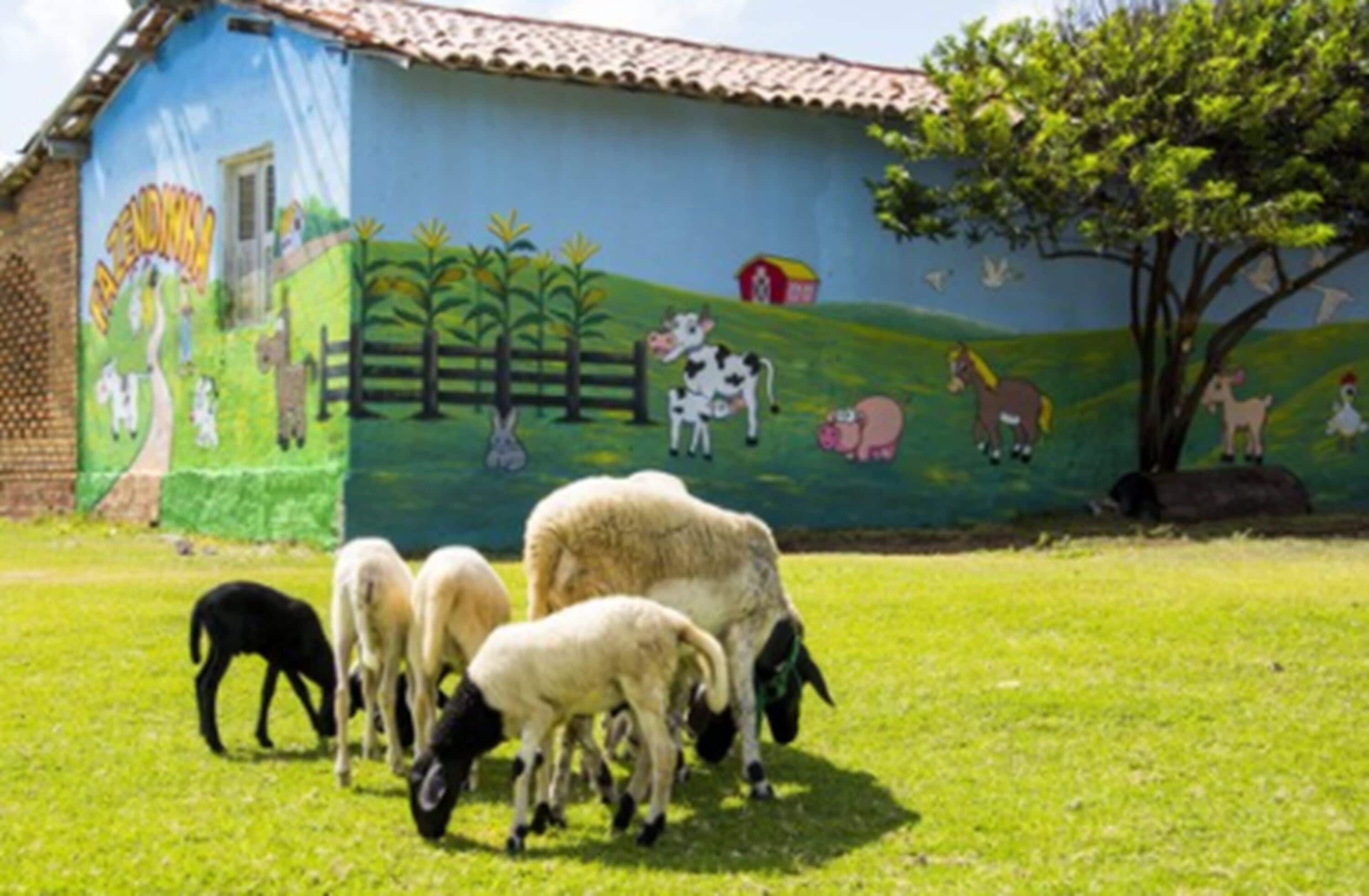 A mural on a building depicting farm animals and a tree.